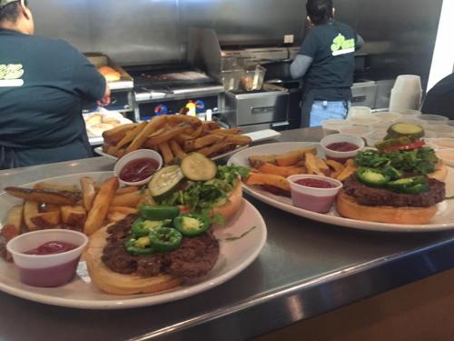 Two plates of burgers with toppings, served with fries and dipping sauces, in a casual dining setting.