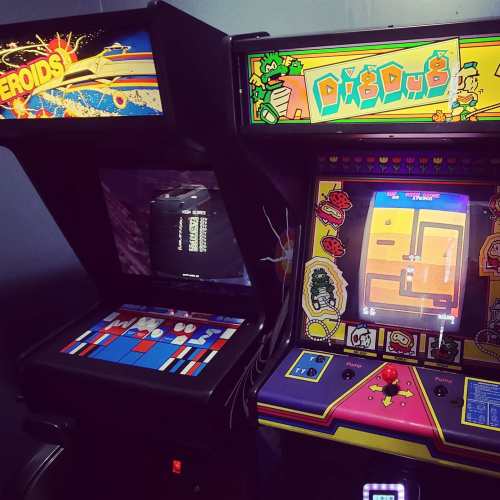 Two vintage arcade game machines: "Asteroids" on the left and "Dig Dug" on the right, featuring colorful screens and controls.