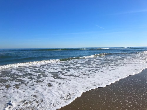 A serene beach scene with gentle waves lapping at the shore under a clear blue sky.