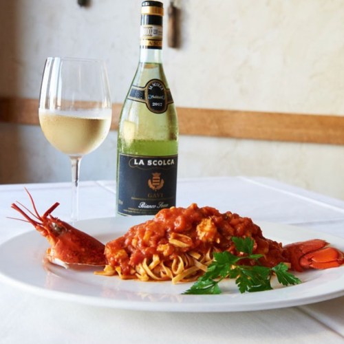 A plate of pasta with seafood in tomato sauce, garnished with parsley, alongside a glass of white wine and a bottle.