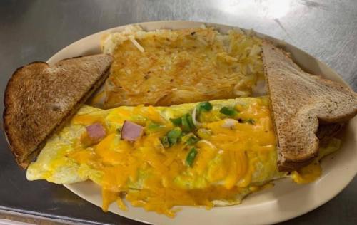 A plate featuring a cheese omelet with ham and green onions, crispy hash browns, and two slices of toasted bread.