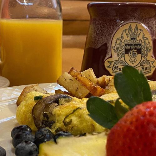 A close-up of a breakfast plate with an omelet, potatoes, berries, and a mug beside a glass of orange juice.