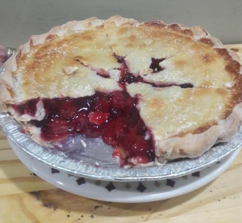 A cherry pie with a golden crust, partially sliced, revealing a vibrant red filling inside.