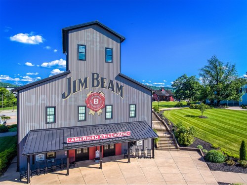 Exterior view of the Jim Beam American Stillhouse, featuring a large sign and well-maintained landscaping under a blue sky.