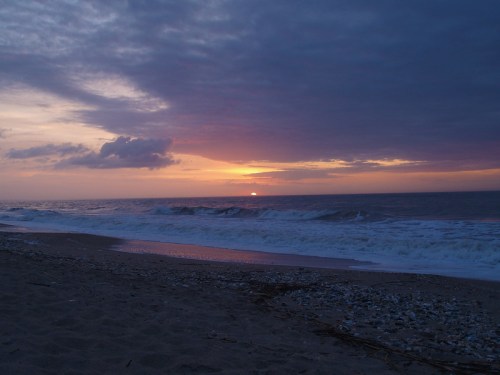 A serene beach at sunset, with gentle waves and a colorful sky filled with clouds.