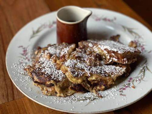A plate of golden-brown French toast dusted with powdered sugar, accompanied by a small pitcher of syrup.
