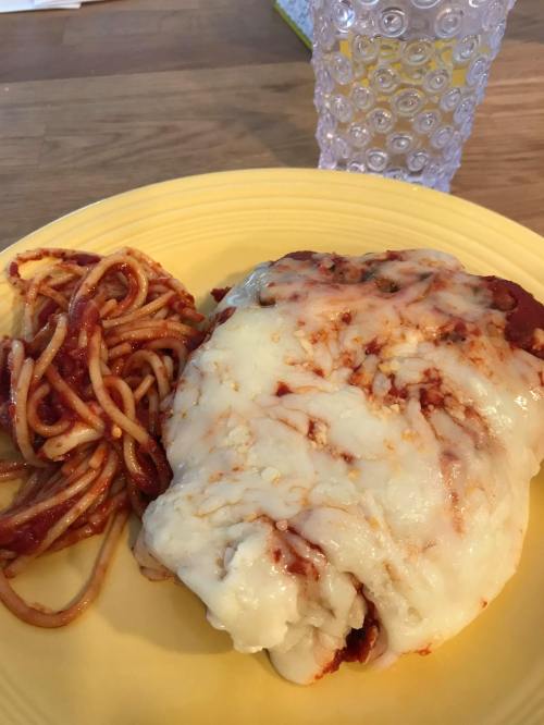 A plate with a large cheese-covered dish and a side of spaghetti in marinara sauce, next to a clear glass of water.