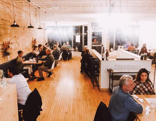 A cozy restaurant interior with diners at tables, warm lighting, and a modern design featuring wooden floors and brick walls.