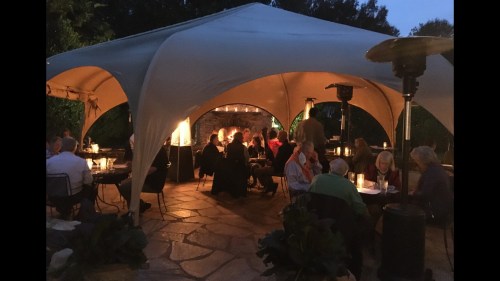 A cozy outdoor dining area under a tent, with guests enjoying dinner in soft evening light.