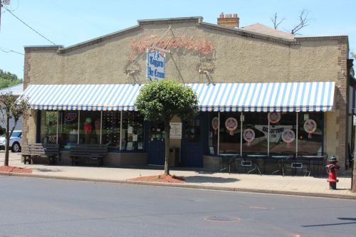 A charming ice cream shop with a striped awning, outdoor seating, and colorful signage on a sunny street.