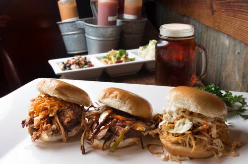 Three delicious sandwiches on a plate, accompanied by sides and a glass of iced tea in a rustic setting.