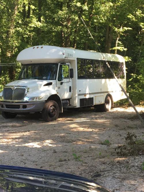 A white bus parked on a gravel area surrounded by trees.