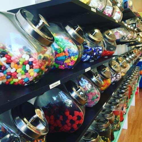 A colorful display of glass jars filled with various candies on black shelves.