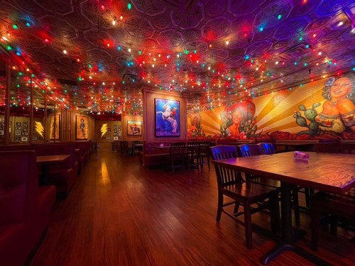 Colorful lights adorn a vibrant restaurant interior with artistic murals and wooden tables.