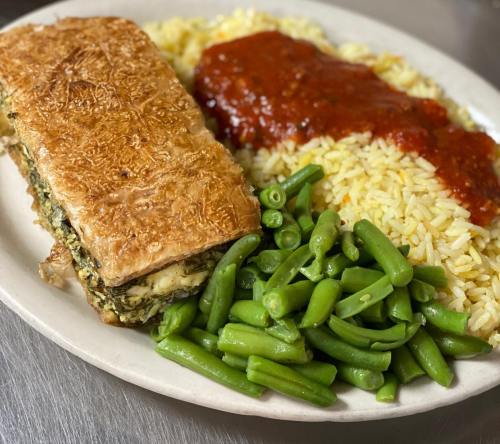 A plate featuring a baked dish, yellow rice with sauce, and a side of green beans.