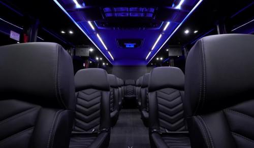 Interior of a luxury bus featuring black leather seats and ambient blue lighting.