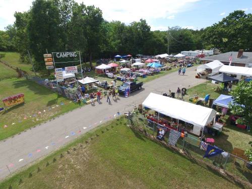 Aerial view of a bustling outdoor market with tents, vendors, and visitors enjoying a sunny day.