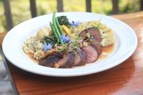 A gourmet plate featuring sliced beef, vegetables, and a creamy side, garnished with edible flowers.