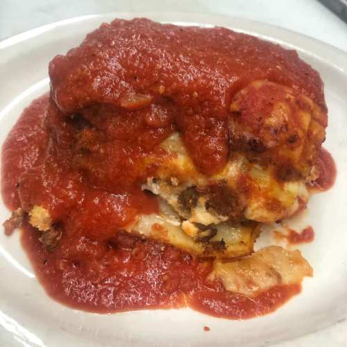 A serving of lasagna topped with rich marinara sauce on a white plate.