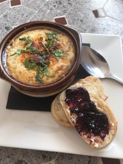 A bowl of creamy dish topped with herbs, served with a slice of bread spread with jam on a white plate.
