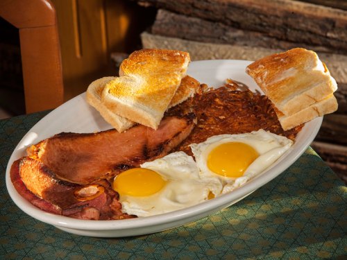 A plate of breakfast featuring two fried eggs, ham, hash browns, and toasted bread.