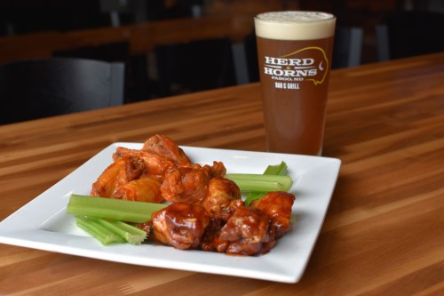 A plate of spicy chicken wings with celery sticks, alongside a glass of beer on a wooden table.