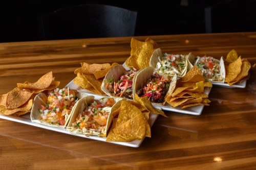 A platter of tacos with various toppings and crispy tortilla chips on a wooden table.