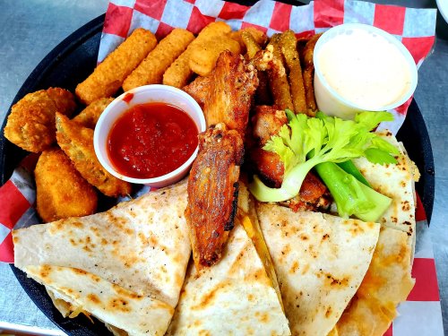 A platter featuring chicken wings, mozzarella sticks, fried pickles, and quesadillas with dipping sauces.