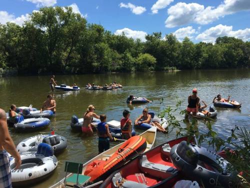 A group of people enjoying a sunny day on the river, floating on inflatable rafts and boats surrounded by greenery.