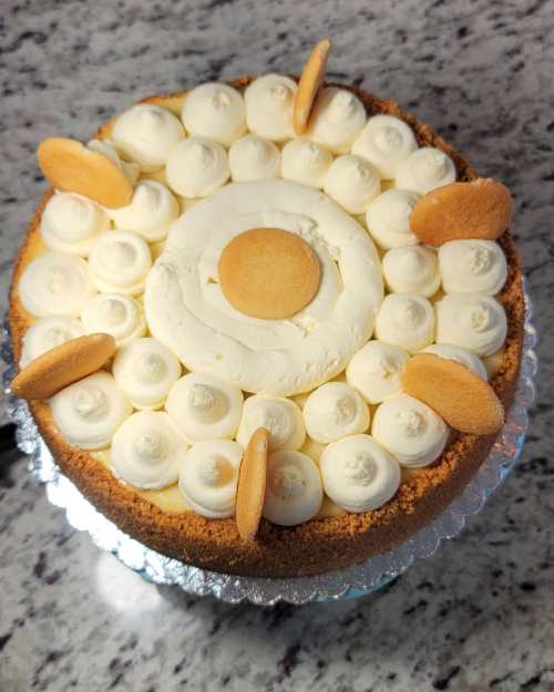 A round cake topped with cream swirls and vanilla wafers on a silver platter, set against a granite countertop.