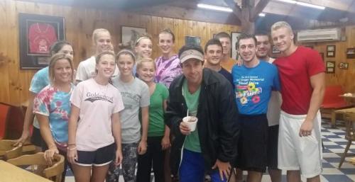A group of smiling people poses together in a cozy, wooden interior, enjoying a casual gathering.
