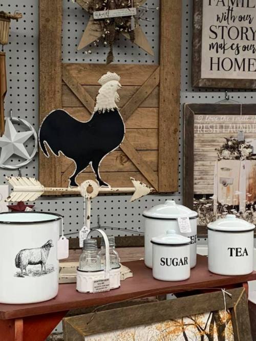 A rustic display featuring a black rooster silhouette, vintage decor, and white canisters labeled "SUGAR" and "TEA."