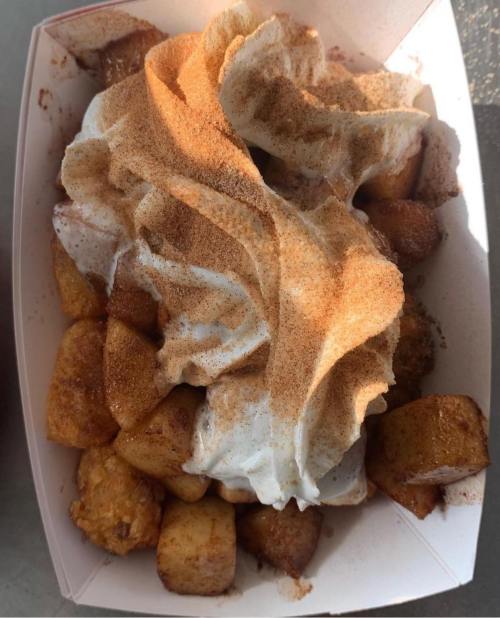 A container filled with cinnamon-coated fried potatoes topped with whipped cream and a dusting of cinnamon.
