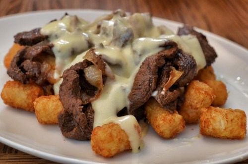 A plate of crispy tater tots topped with sliced beef and melted cheese sauce.