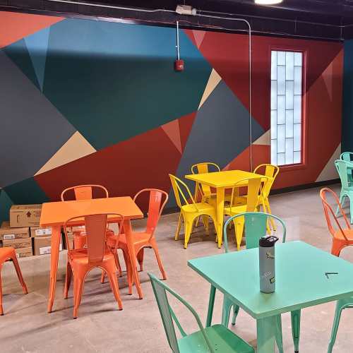 Colorful café interior featuring orange and green tables and chairs against a geometric patterned wall.
