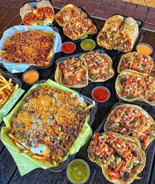 A vibrant spread of tacos, burritos, nachos, and fries, accompanied by various colorful sauces in small cups.