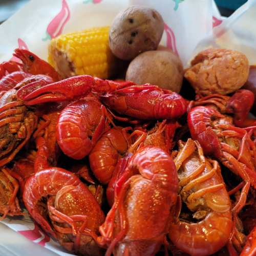 A close-up of a seafood dish featuring red crawfish, corn on the cob, and small potatoes in a bowl.