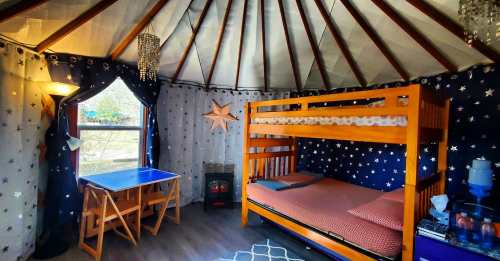 Cozy yurt interior with a bunk bed, blue table, starry curtains, and a warm atmosphere.