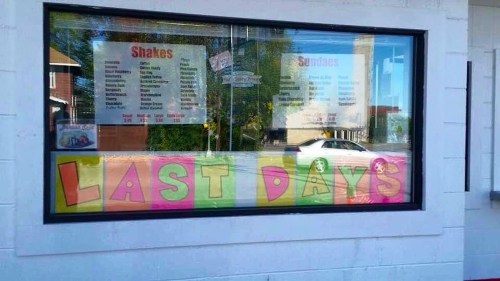 A window display with colorful letters spelling "LAST DAYS" alongside a menu for shakes and sundaes.