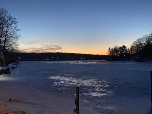 A serene winter scene of a frozen lake at dusk, with a colorful sunset and trees lining the shore.