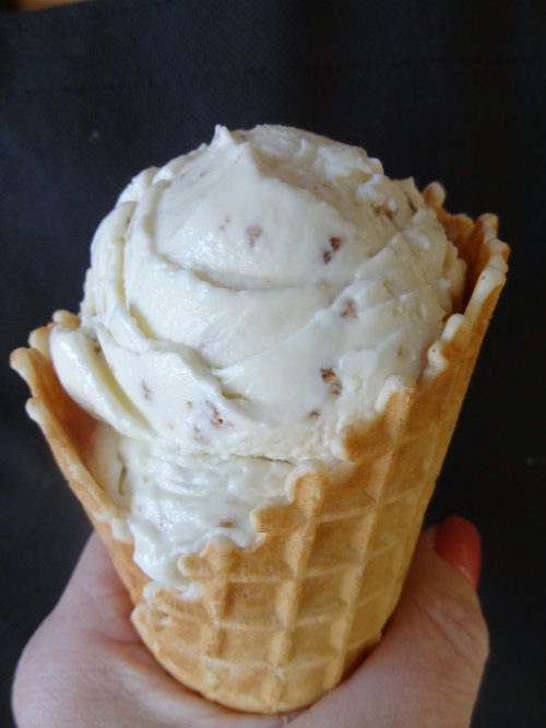A hand holding a waffle cone filled with creamy vanilla ice cream swirled with chocolate bits.