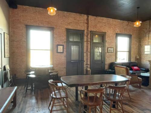 Cozy room with exposed brick walls, wooden furniture, and large windows, featuring a table and chairs.