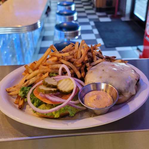 A plate featuring a cheeseburger with lettuce, pickles, and onions, accompanied by crispy fries and a dipping sauce.