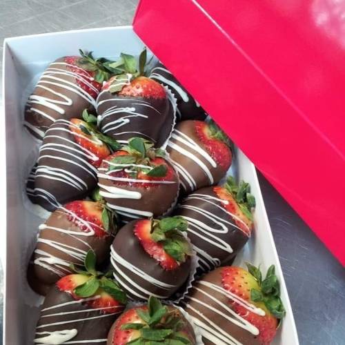 A box of chocolate-covered strawberries drizzled with white chocolate, arranged neatly inside a pink box.