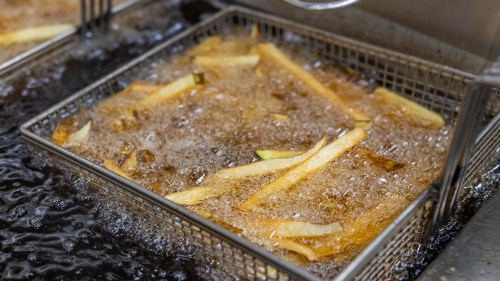 A basket of French fries frying in bubbling oil in a deep fryer.