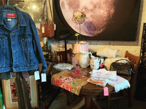 A vintage table displays a denim jacket, handbags, decorative items, and various textiles against a moon backdrop.