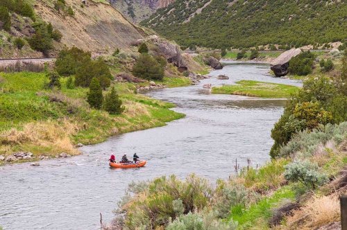 Two people in an orange raft navigate a winding river surrounded by lush greenery and rocky hills.