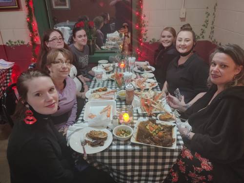A group of seven women enjoying a meal together at a restaurant, with seafood and drinks on the table.