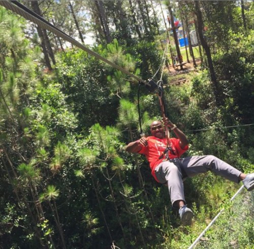 A person in a red shirt zip-lining through a forested area, smiling and enjoying the adventure.