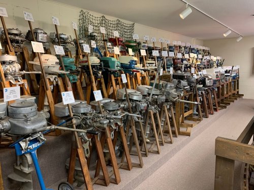 A display of various vintage outboard motors arranged on stands in a museum-like setting.